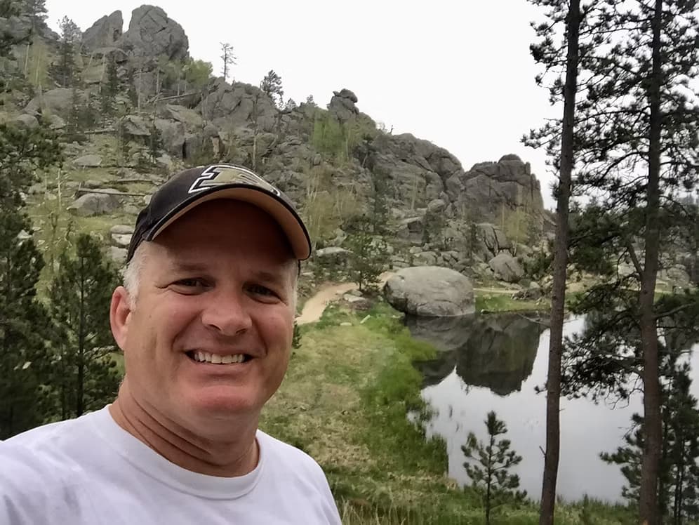 Joe Kuhn smiling on a hiking trail beside a lake